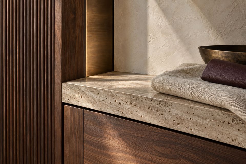 Close-up of a honed travertine top over walnut drawers with fluted timber panelling and a folded linen throw